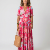 Woman wearing a pink floral short-sleeve V-neck midi dress holding a tan leather tote bag.