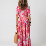 Rear view of a woman wearing a pink floral short-sleeve midi dress, holding a tan leather tote bag.