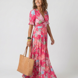Model wearing a pink floral midi dress with short sleeves, V-neck, and tiered skirt, holding a tan tote bag.