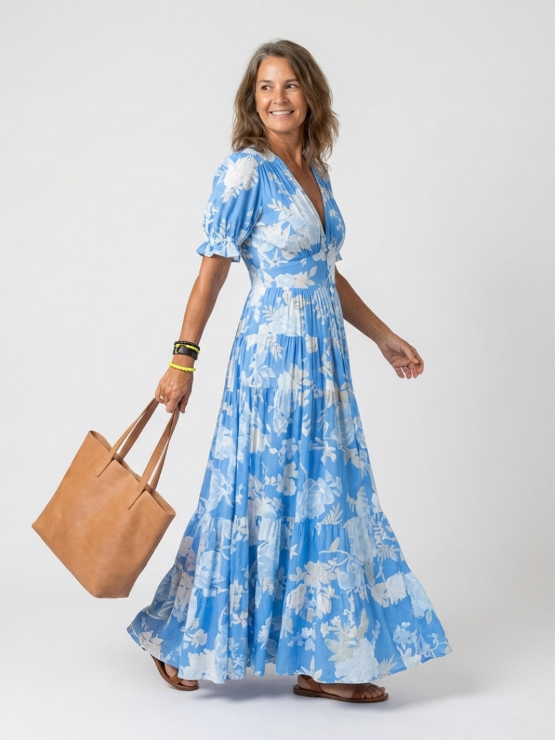 Blue V-neck midi dress with short puff sleeves, white floral print, and tiered skirt, worn with a brown tote.