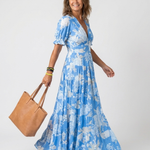 Blue V-neck midi dress with short puff sleeves, white floral print, and tiered skirt, worn with a brown tote.