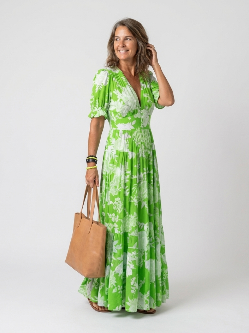 Model wearing a green floral V-neck midi dress with short puff sleeves, holding a tan leather tote bag.