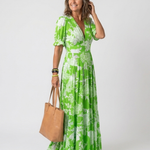 Model wearing a green floral V-neck midi dress with short puff sleeves, holding a tan leather tote bag.