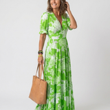 Model wearing a green floral V-neck midi dress with short puff sleeves, holding a tan leather tote bag.